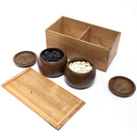 Open kiri wood box with two opened itami goke (go stone bowls) in front of it. The left bowl holds river slate (black) goishi (go stones) and the right bowl holds clamshell (white) goishi.