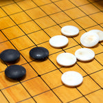 River slate (black) and clamshell (white) goishi (go stones) on an itame kaya goban (go board).